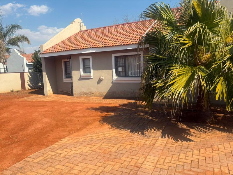 Front exterior view of a single-story house featuring a terracotta tiled roof, paved driveway, and boundary wall with security fencing.