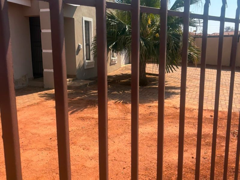 Front view of the property featuring a paved driveway, plastered exterior walls, and a metal security fence.