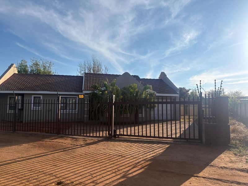 Front elevation of a single-story house featuring a tiled roof, paved driveway, and secure metal perimeter fencing with integrated electric security wires.