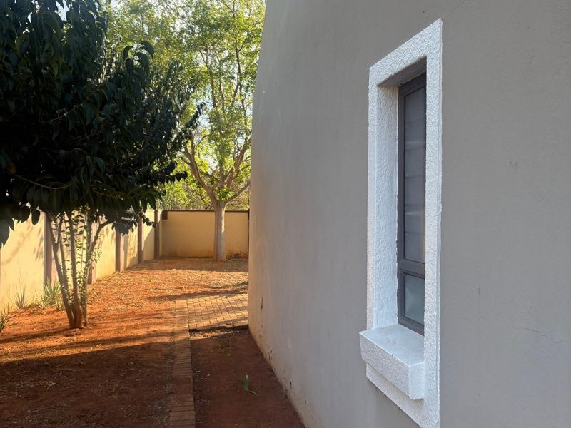 A view of the side exterior of the house featuring a paved walkway, boundary wall, and a window with a textured white surround.