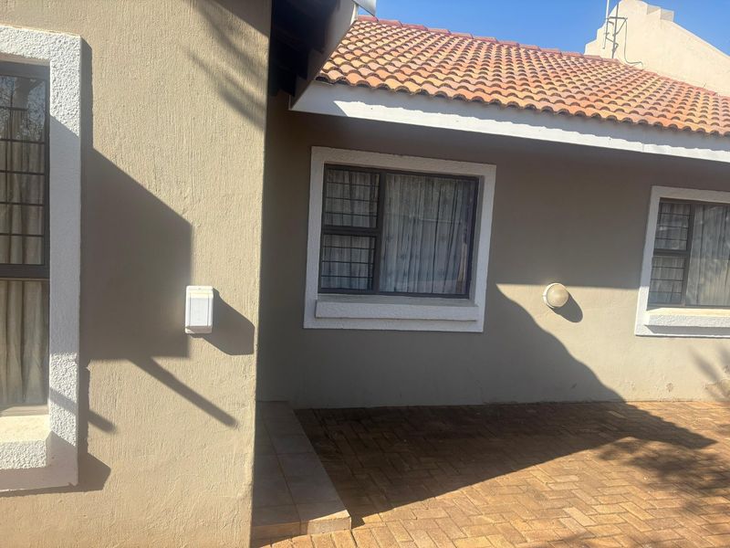A view of the rear exterior of the house featuring a paved patio area, terracotta roof tiles, and windows with security bars.