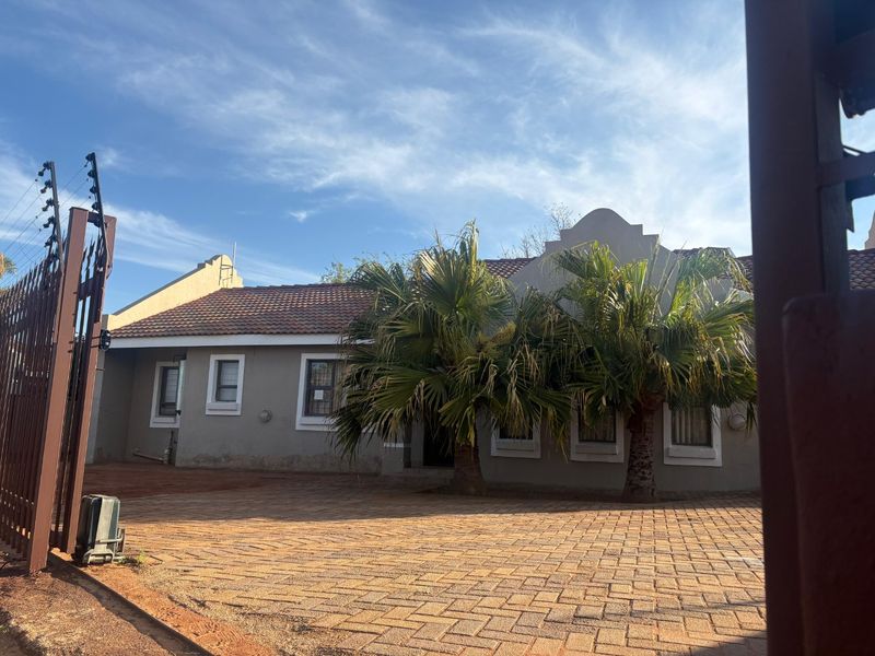 Front view of the property featuring a paved driveway, plastered exterior walls, tiled roof, and perimeter electric fencing.