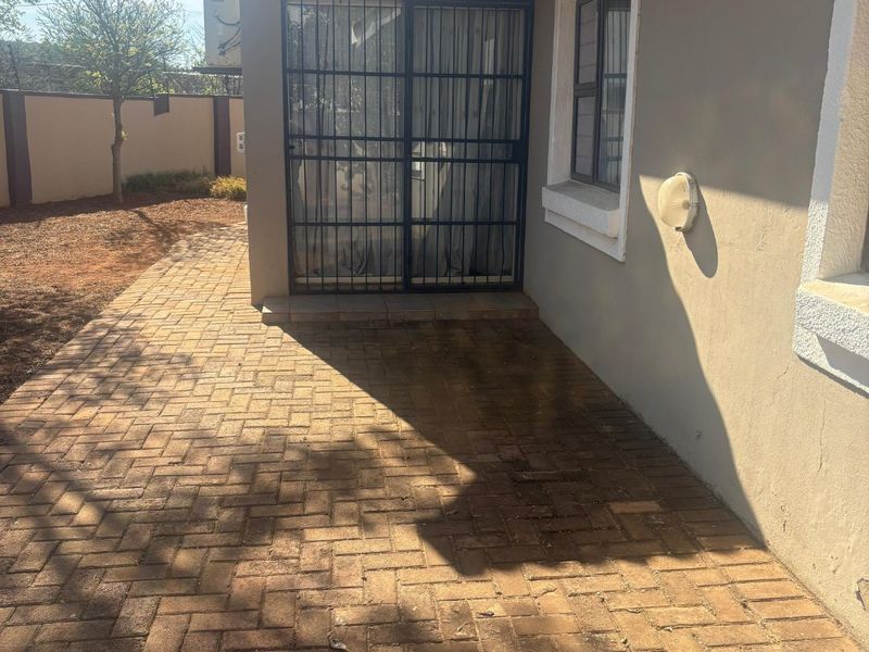 A rear exterior view featuring a paved patio area, a sliding door with a security gate, and a tiled roof.