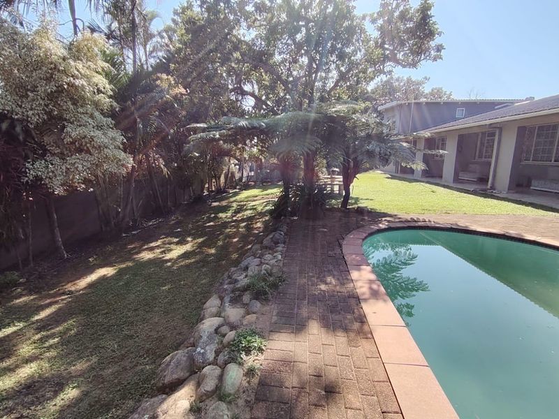 A backyard area featuring a swimming pool with brick paving, a stone retaining wall, and a covered patio adjacent to the house.