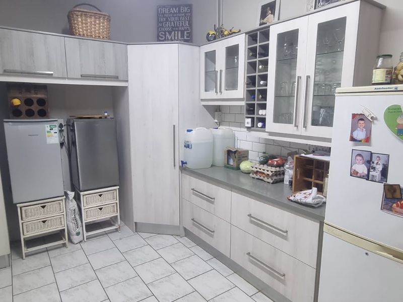 A functional kitchen featuring light wood-grain cabinetry, subway tile backsplash, and ample storage with integrated wine rack and glass-fronted display cabinets.
