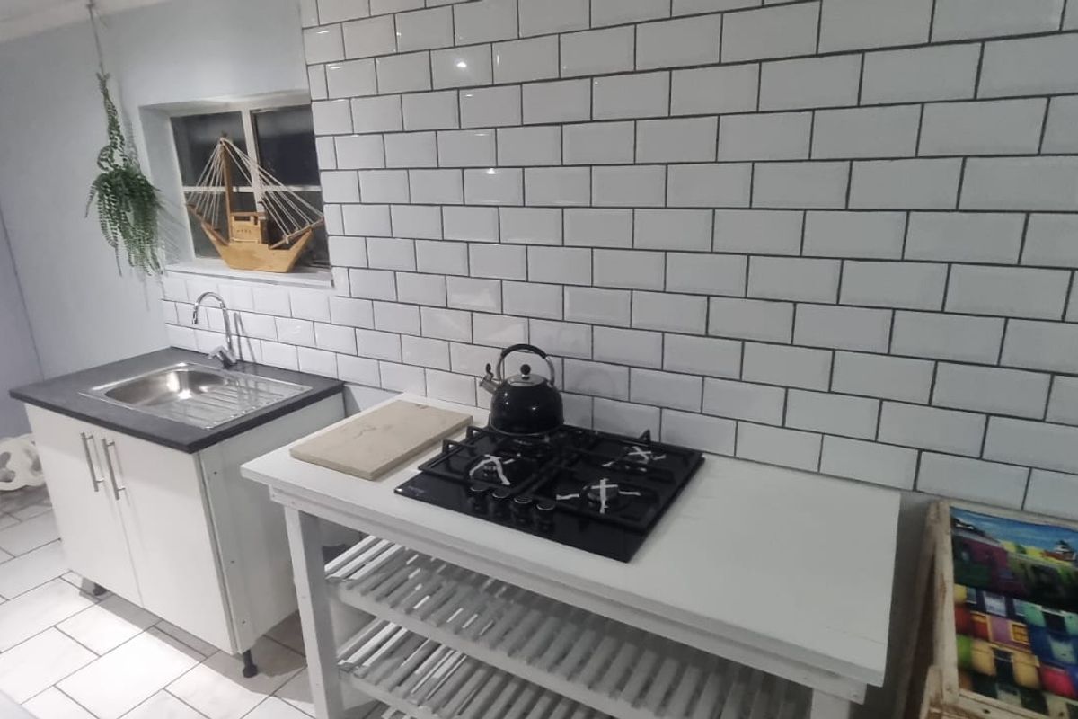A functional kitchen area featuring a gas hob, subway tile backsplash, and a stainless steel sink with base cabinetry.