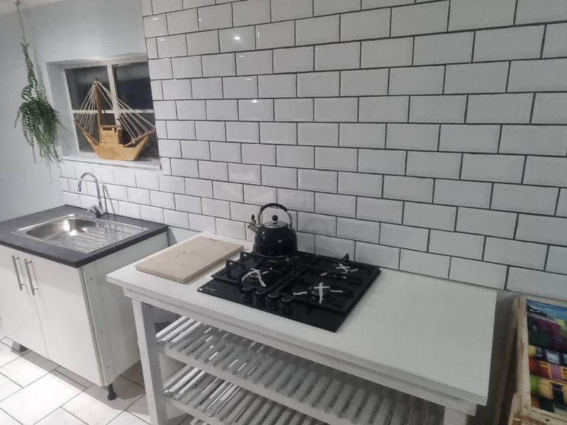 A functional kitchen area featuring a gas hob, subway tile backsplash, and a stainless steel sink with base cabinetry.