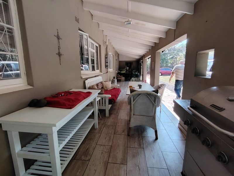 A covered outdoor patio area featuring wood-look tiled flooring, exposed beam ceilings, and a built-in barbecue, providing a functional space for outdoor entertaining.
