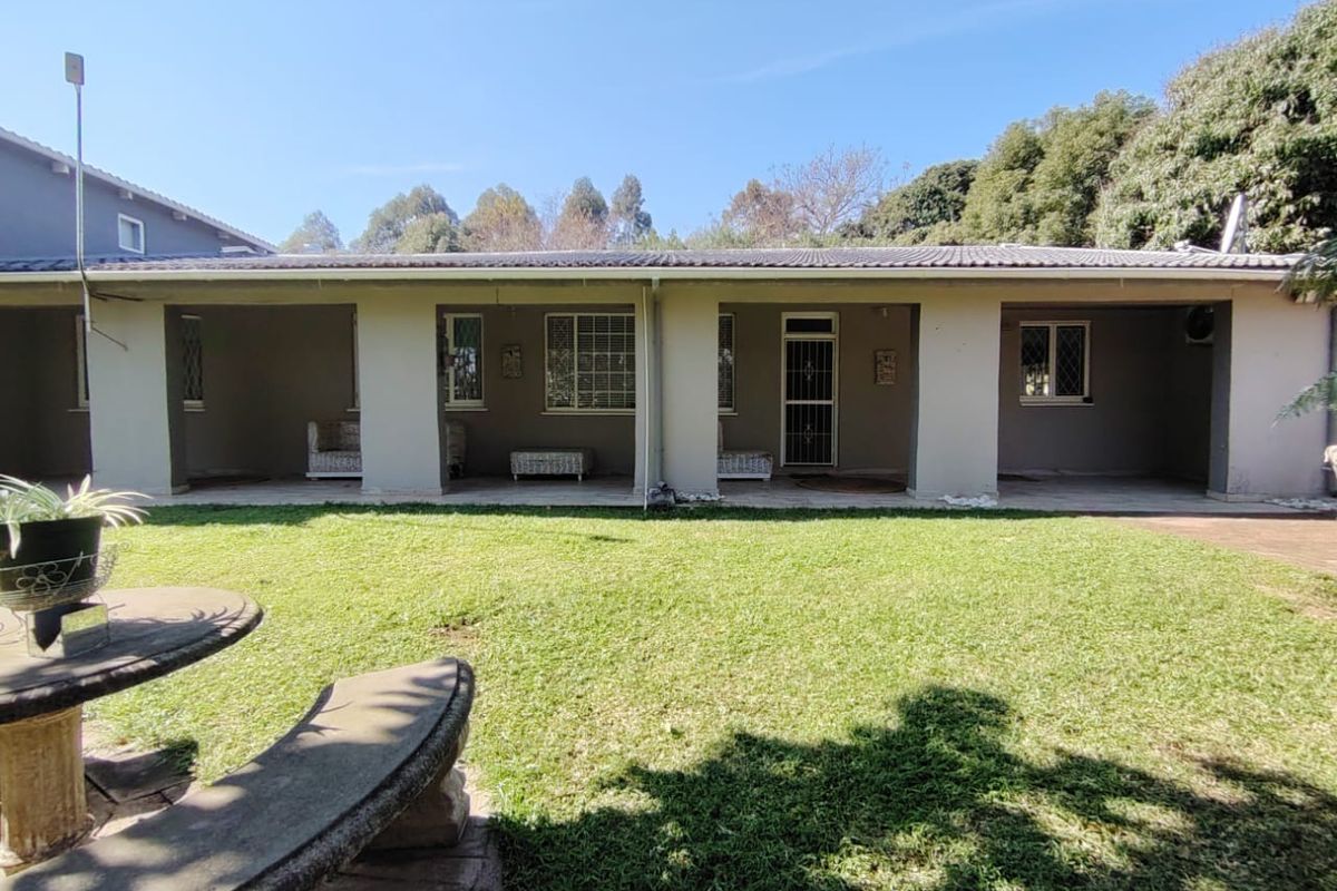 A spacious rear exterior view featuring a covered patio area, tiled roof, and a well-maintained lawn.