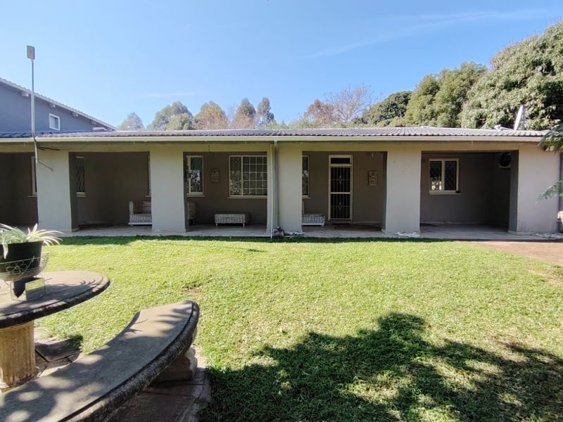 A spacious rear exterior view featuring a covered patio area, tiled roof, and a well-maintained lawn.