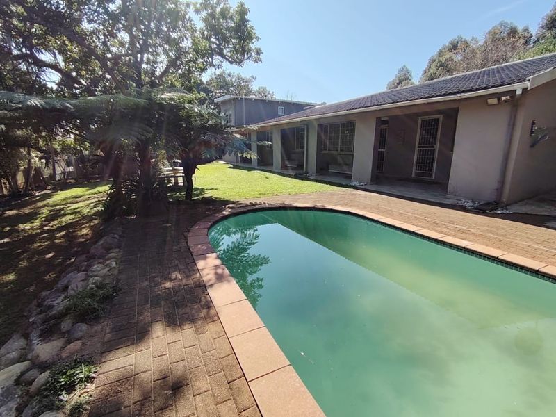 Rear garden area featuring a swimming pool, brick paved surround, and a covered patio attached to the main house structure.