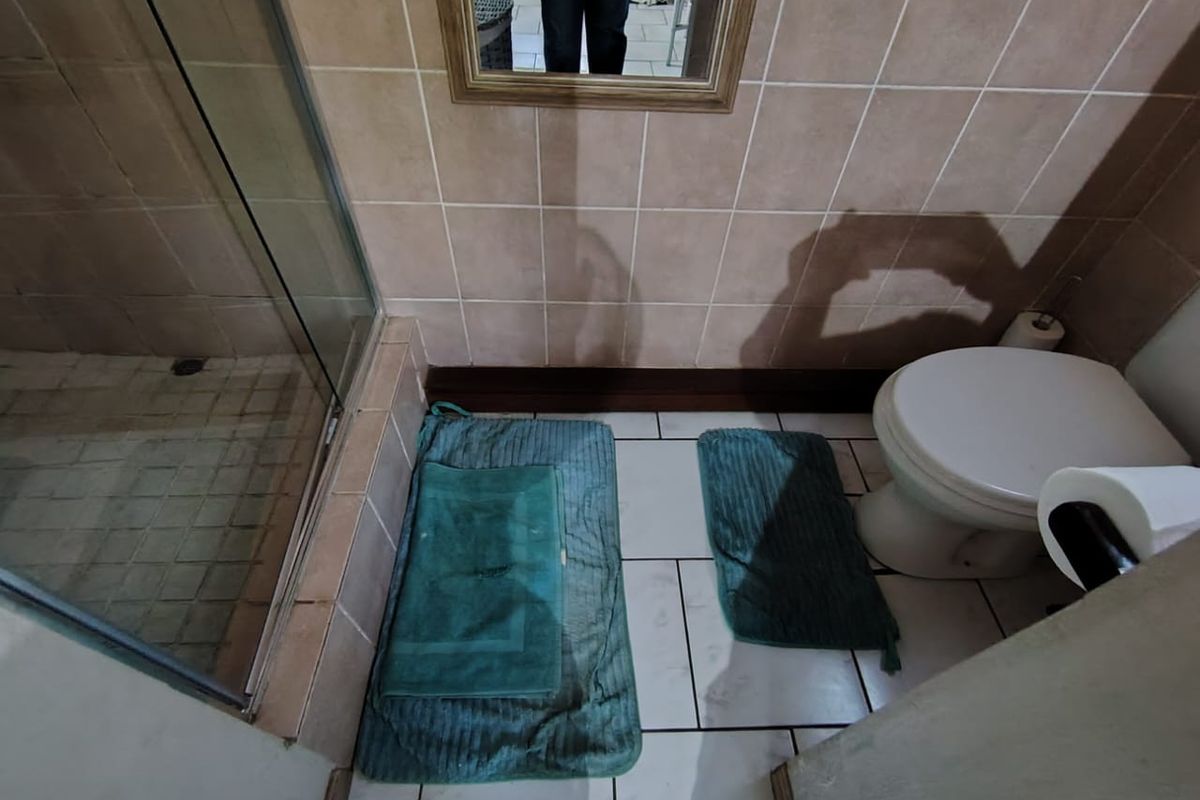 A compact bathroom featuring a shower enclosure, toilet, and tiled finishes. The space requires cosmetic updates to improve its overall condition and appeal.