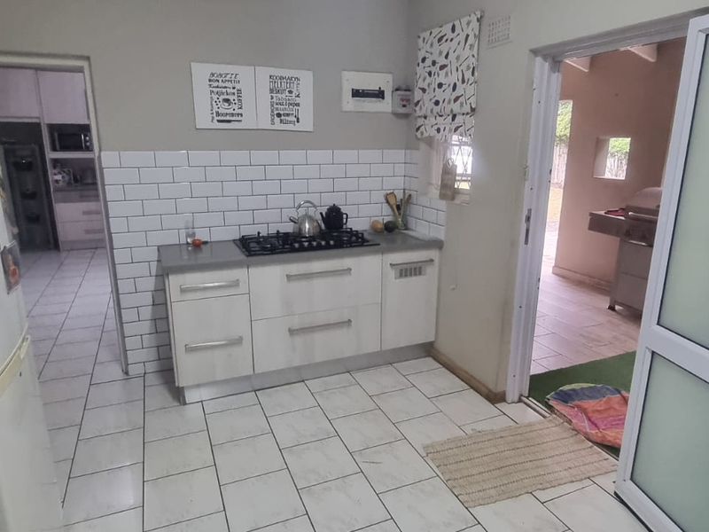 A functional kitchen featuring white cabinetry, a gas hob, subway tile backsplash, and tiled flooring, with direct access to an outdoor area.