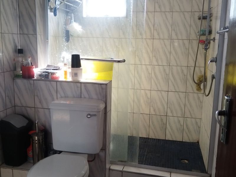 A functional bathroom featuring a tiled shower enclosure, a standard toilet, and tiled flooring with natural light from a small window.