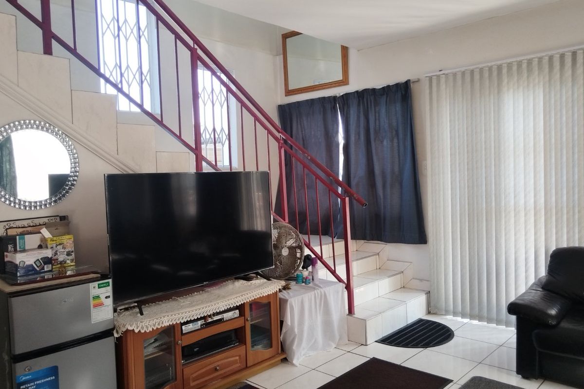 A living area featuring tiled flooring, a staircase with a metal railing, and vertical blinds leading to an outdoor space.