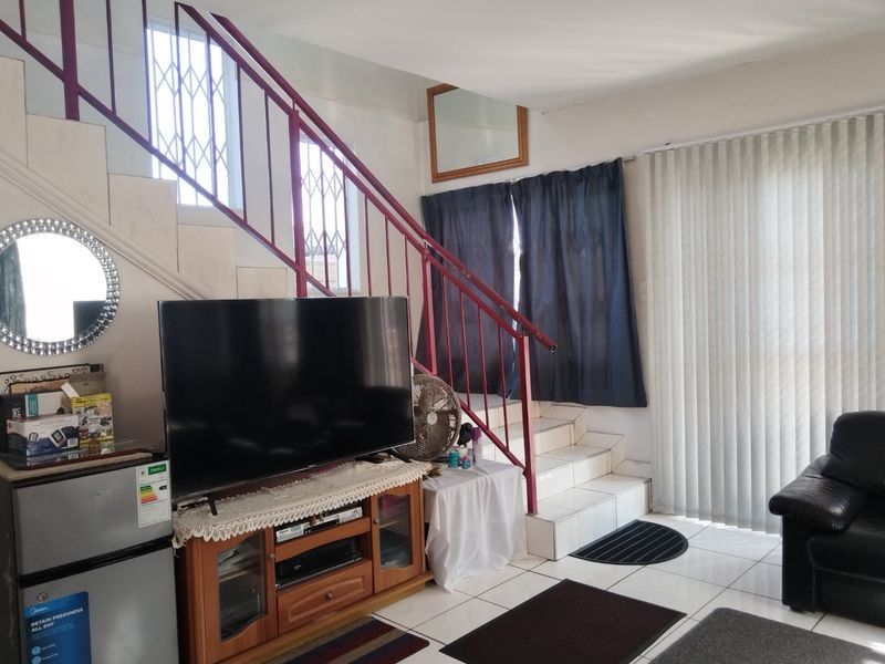 A living area featuring tiled flooring, a staircase with a metal railing, and vertical blinds leading to an outdoor space.