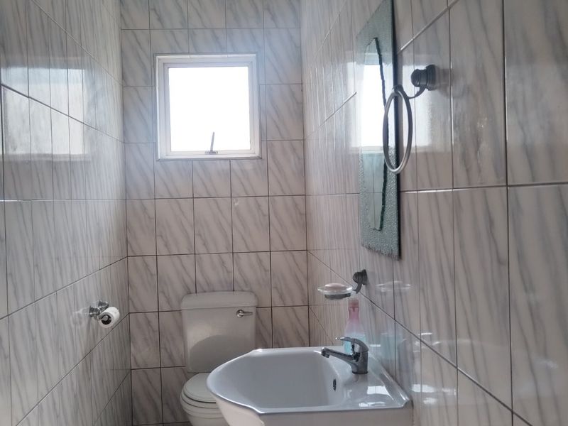 A compact bathroom featuring fully tiled walls, a vanity basin, and a standard toilet.