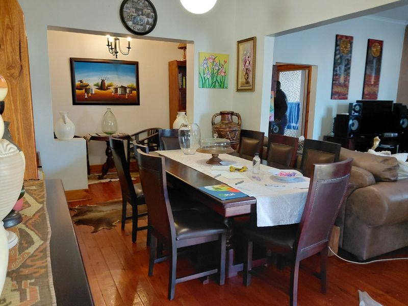 A dining room featuring polished hardwood flooring and an open-plan layout with an archway leading to an adjacent living area.