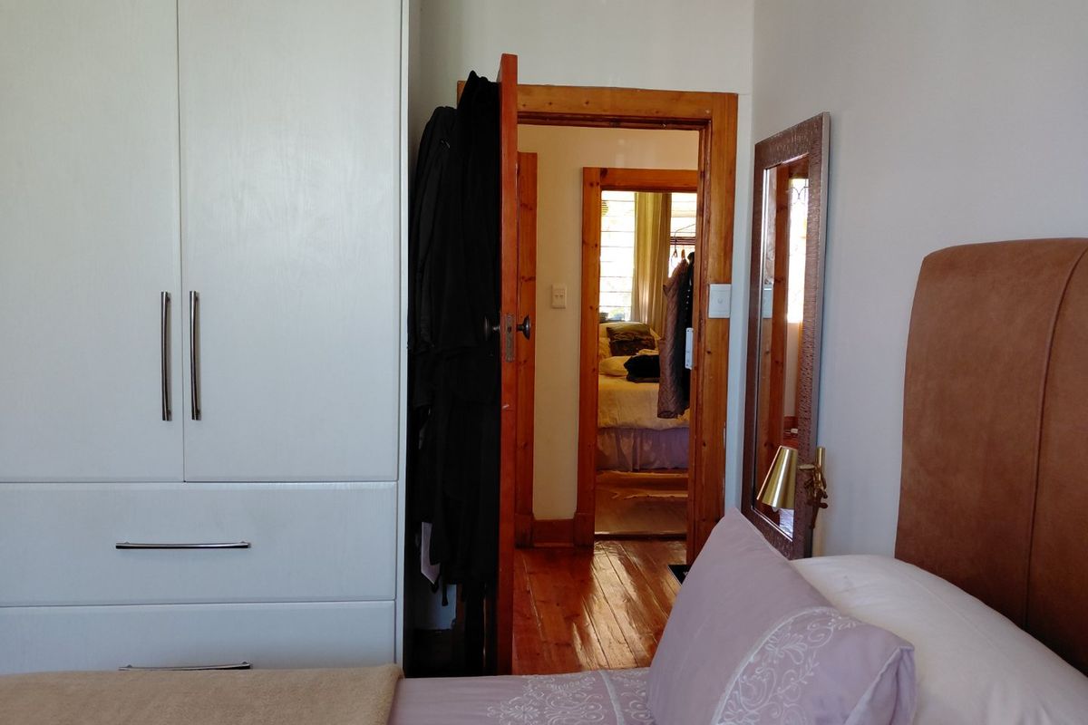 A bedroom featuring polished timber flooring, a built-in white wardrobe, and a wooden door frame leading to an adjacent room.
