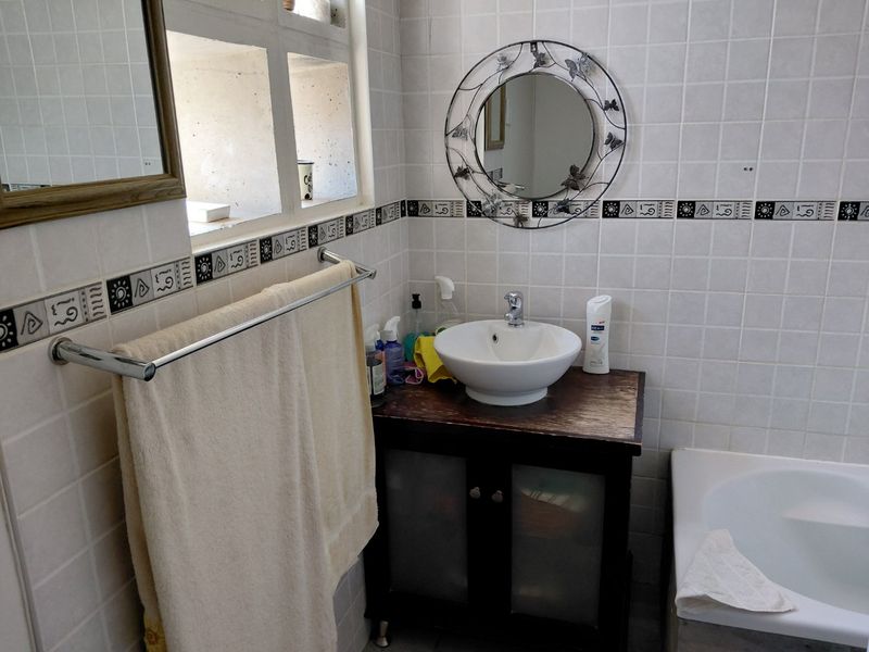 A functional bathroom featuring a vessel sink on a vanity cabinet, tiled walls with a decorative border, and a built-in bathtub.