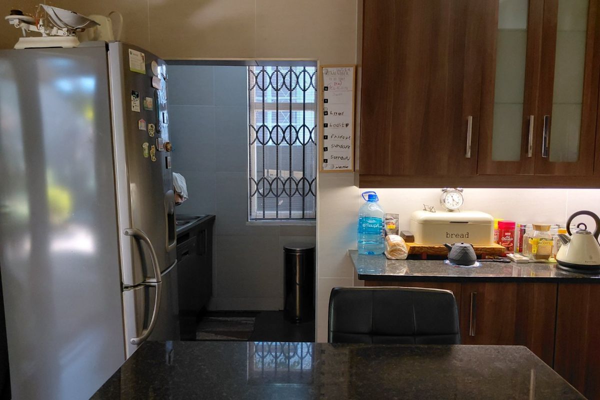 A functional kitchen featuring dark granite countertops, wood-finish cabinetry, and under-cabinet lighting, with an adjacent scullery area visible through the doorway.