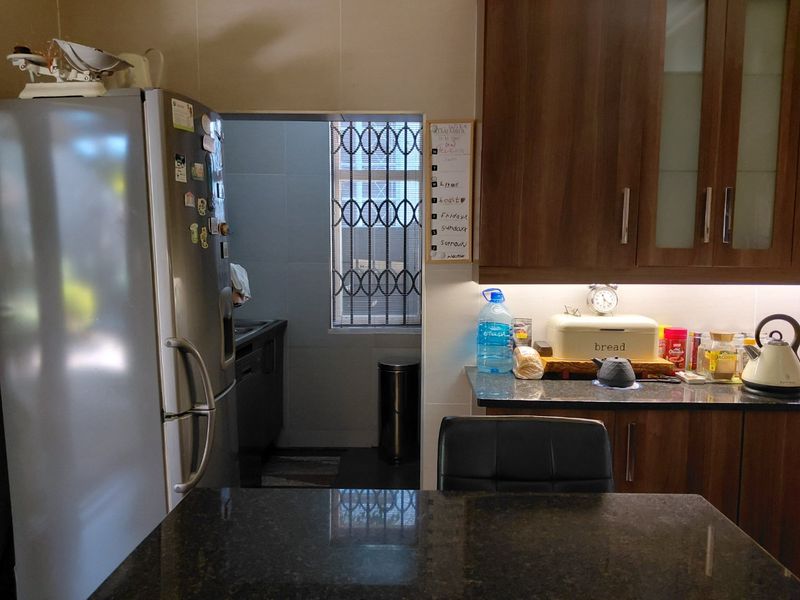 A functional kitchen featuring dark granite countertops, wood-finish cabinetry, and under-cabinet lighting, with an adjacent scullery area visible through the doorway.