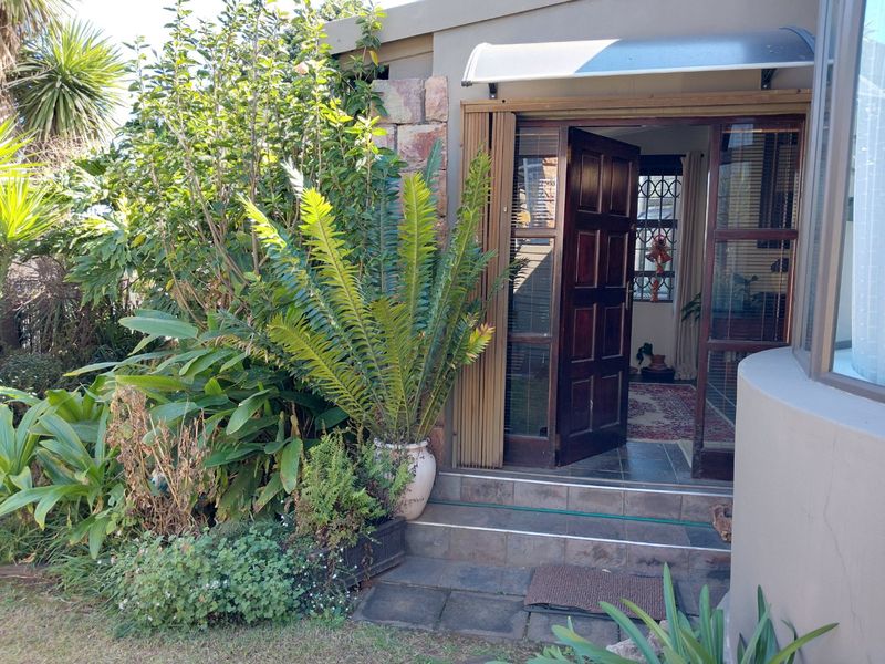Rear entrance featuring stone cladding, tiled steps, and a timber door leading into the home, surrounded by established garden landscaping.