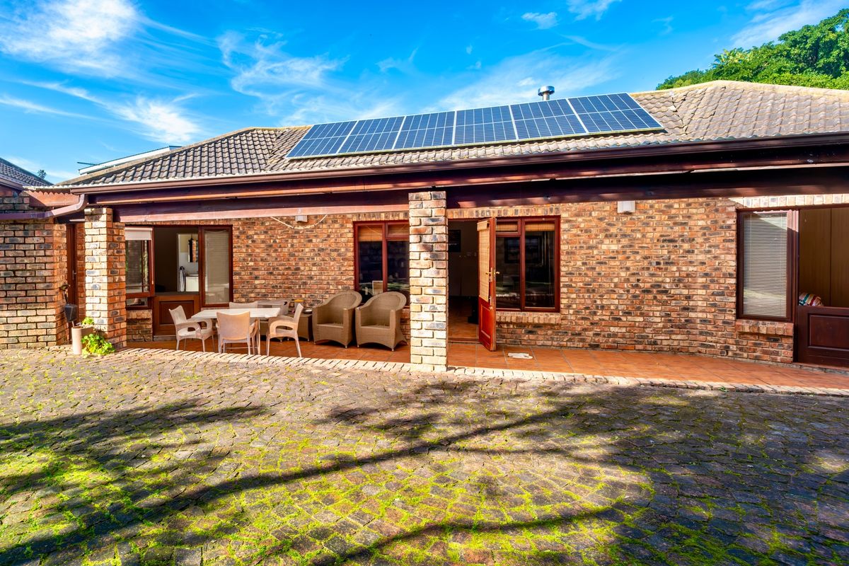 Rear exterior view featuring a brick facade, covered patio area, and roof-mounted solar panels, set against a paved courtyard.