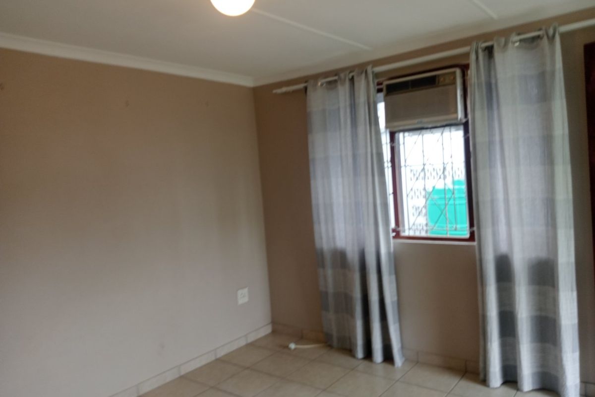 A vacant bedroom featuring tiled flooring, a built-in window air conditioning unit, and security bars on the window.