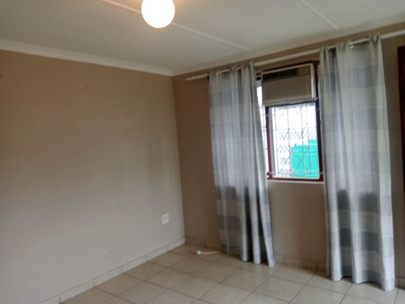 A vacant bedroom featuring tiled flooring, a built-in window air conditioning unit, and security bars on the window.
