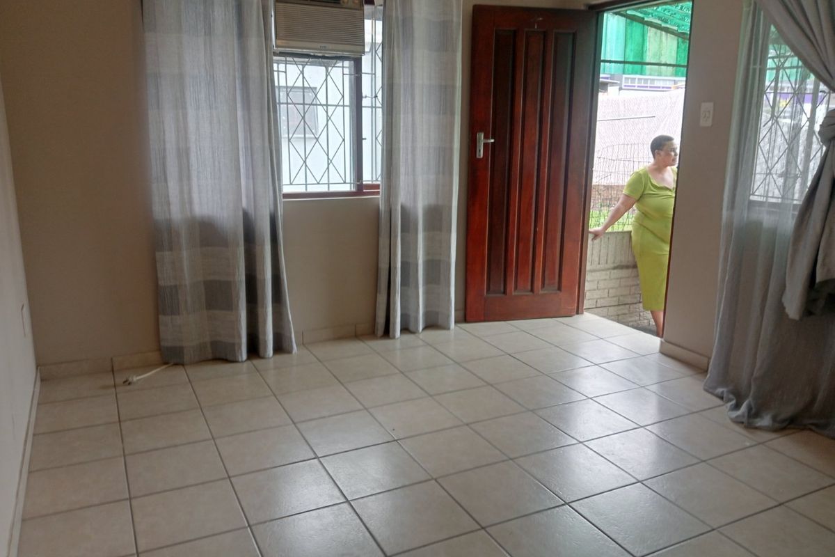 An empty living room featuring tiled flooring, a window-mounted air conditioning unit, and direct access to an outdoor area through a timber door.
