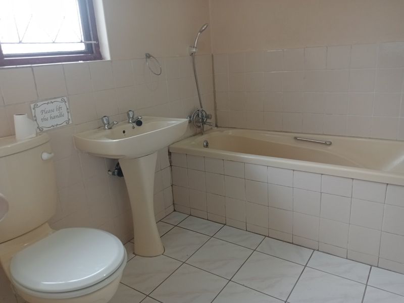 A dated bathroom featuring a pedestal basin, bathtub with handheld shower mixer, and tiled surfaces throughout.