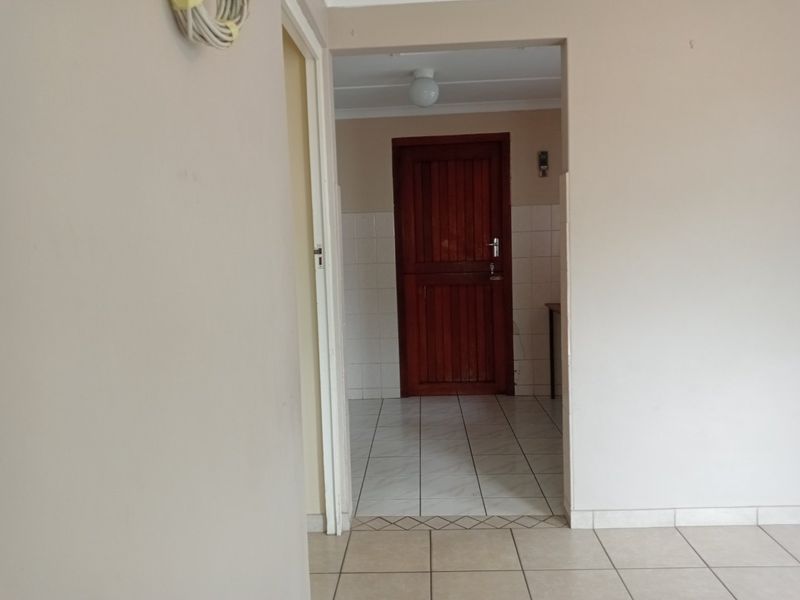 A functional hallway area featuring tiled flooring and a solid timber door, connecting two interior spaces within the apartment.