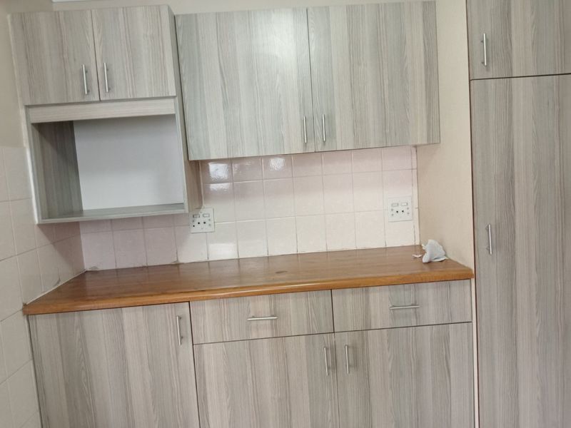 A clean kitchen area featuring light wood-grain laminate cabinetry, a wooden countertop, and a tiled backsplash with integrated electrical outlets.