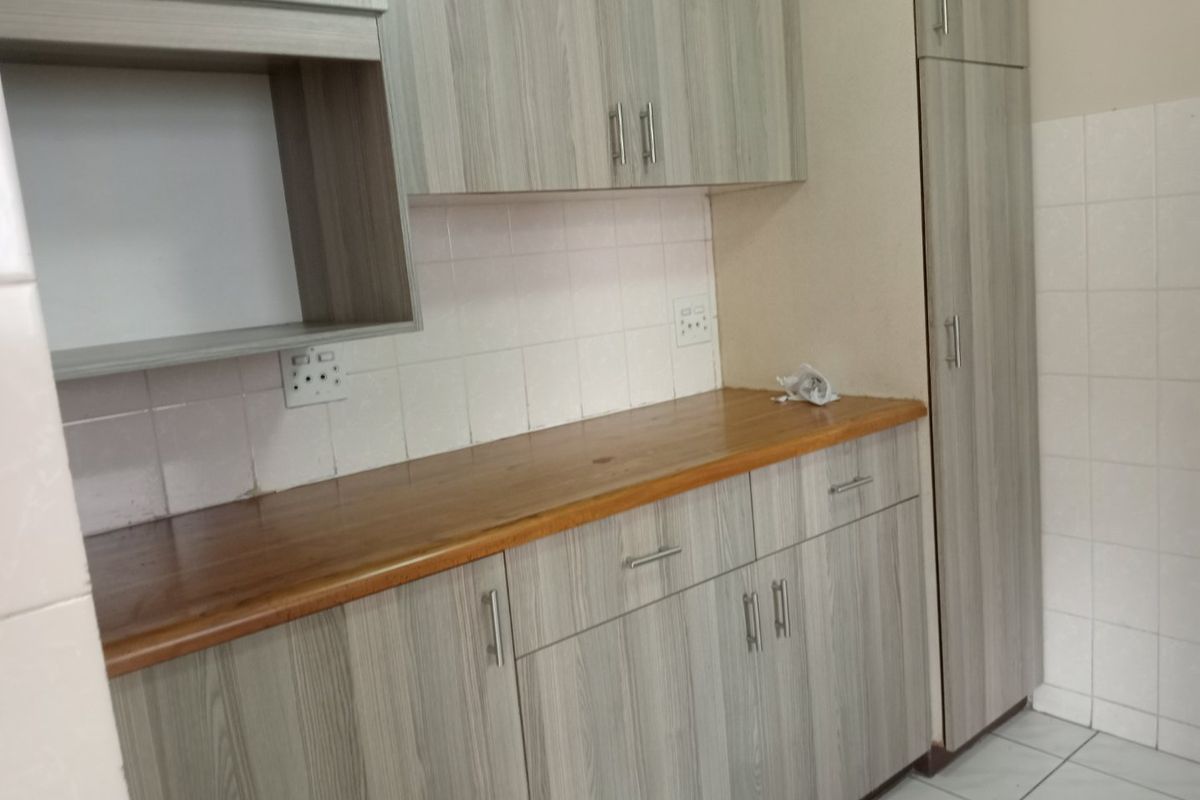 A clean kitchen area featuring modern wood-grain laminate cabinetry, a warm wooden countertop, tiled backsplash, and practical floor tiling with ample storage space.