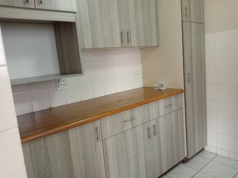A clean kitchen area featuring modern wood-grain laminate cabinetry, a warm wooden countertop, tiled backsplash, and practical floor tiling with ample storage space.