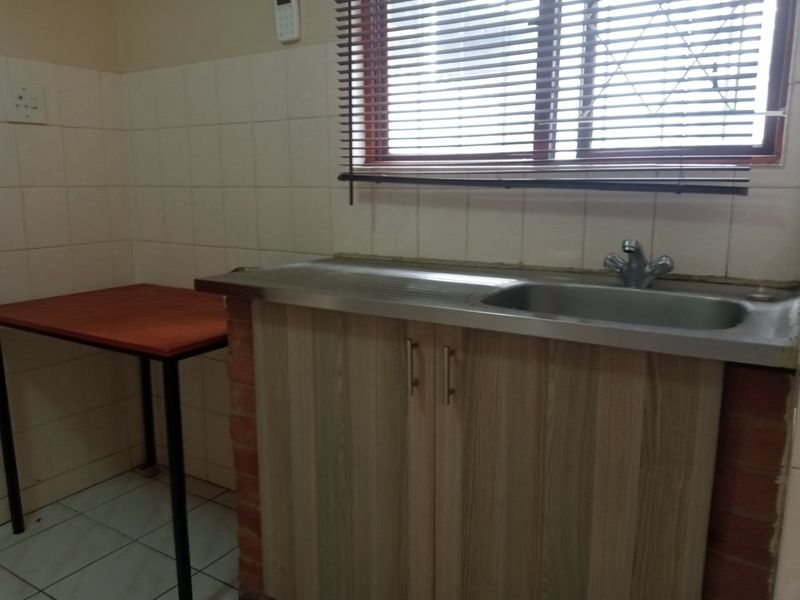 A functional scullery area featuring a stainless steel sink, tiled splashback, and built-in cabinetry with venetian blinds.