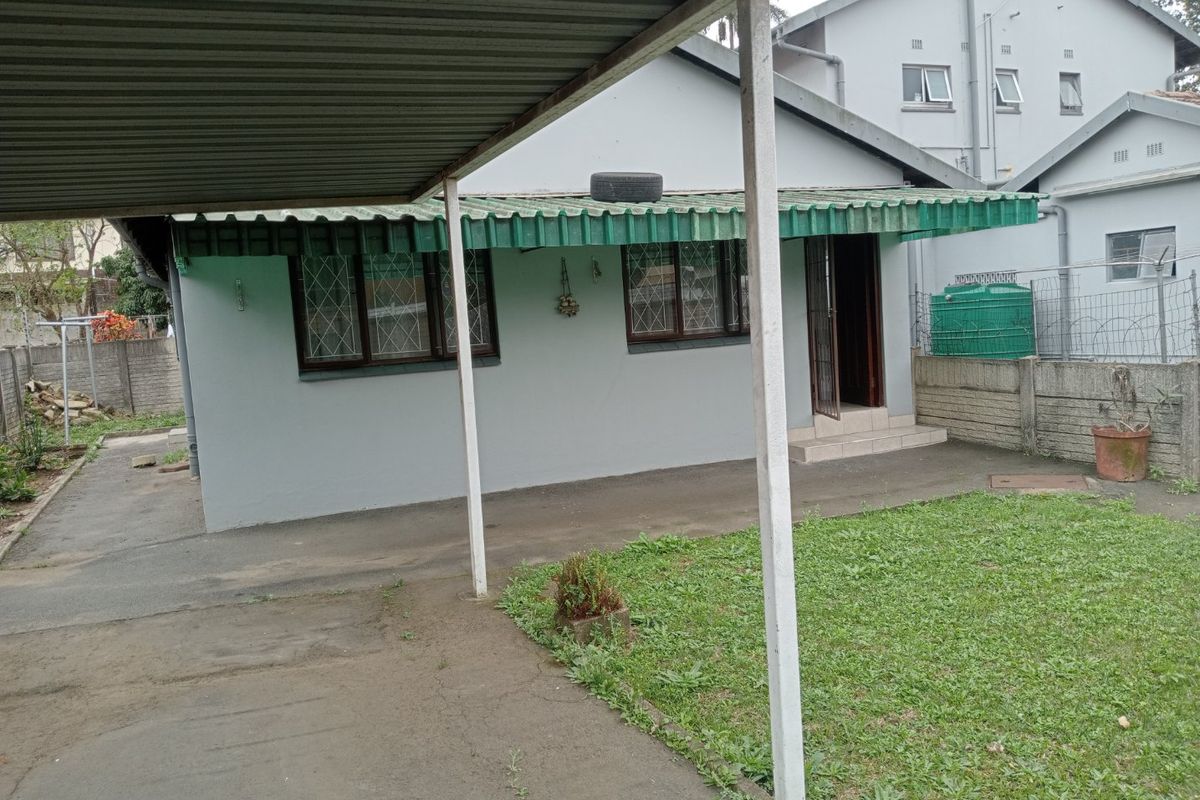 Rear exterior view of the apartment featuring a covered carport, concrete driveway, and a small private garden area with perimeter walling.