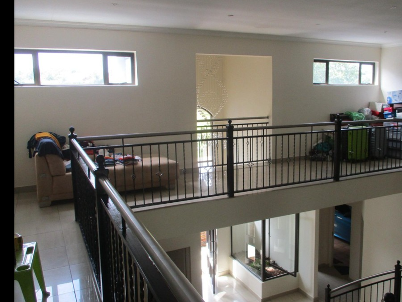 Spacious upper-level landing area featuring a wrought iron balustrade, tiled flooring, and double-volume ceilings overlooking the lower level.