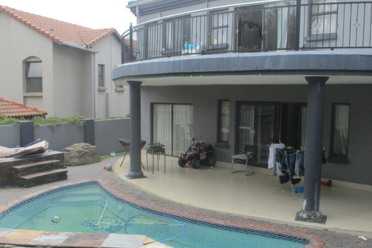 Rear view of the property featuring a covered patio, upper balcony with wrought iron railings, and a swimming pool with safety net.
