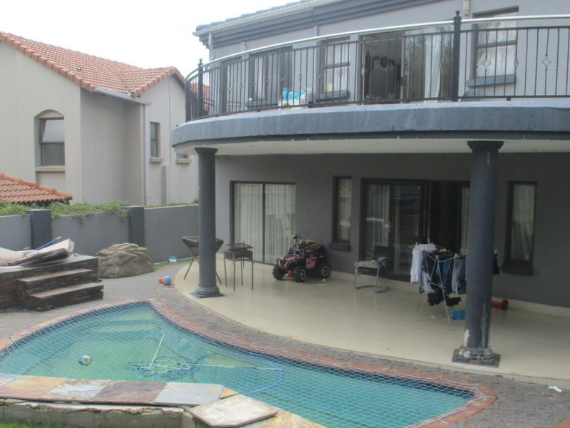 Rear view of the property featuring a covered patio, upper balcony with wrought iron railings, and a swimming pool with safety net.
