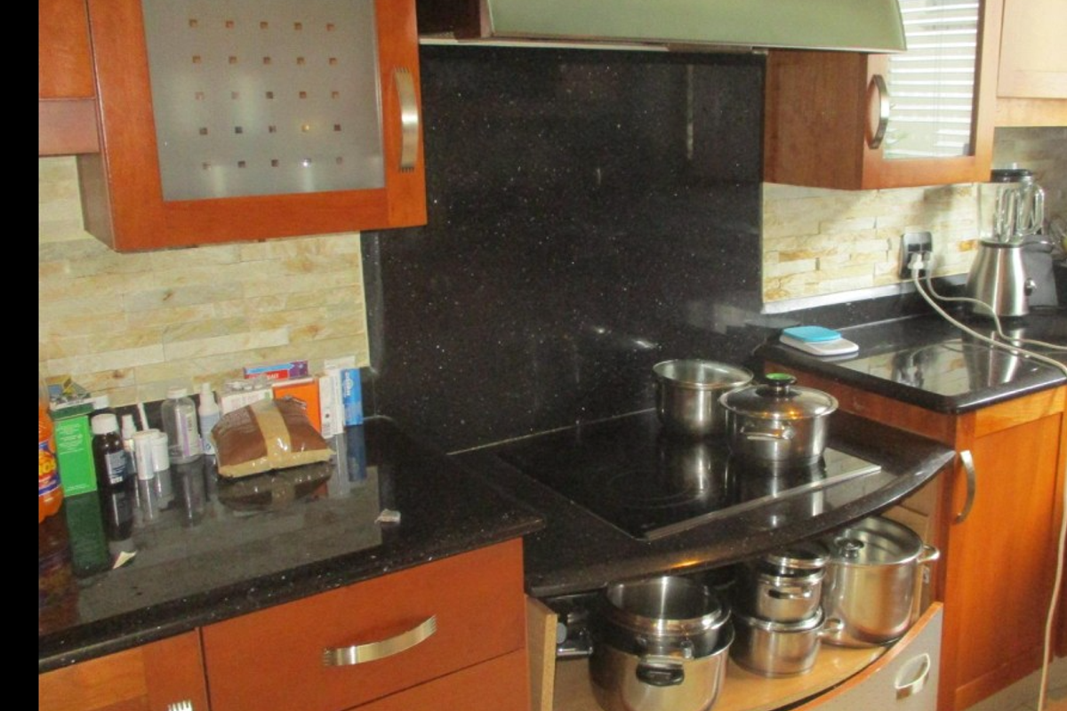 A kitchen area featuring wooden cabinetry, black granite countertops, a stone tile backsplash, and a built-in electric cooktop with an extractor fan.