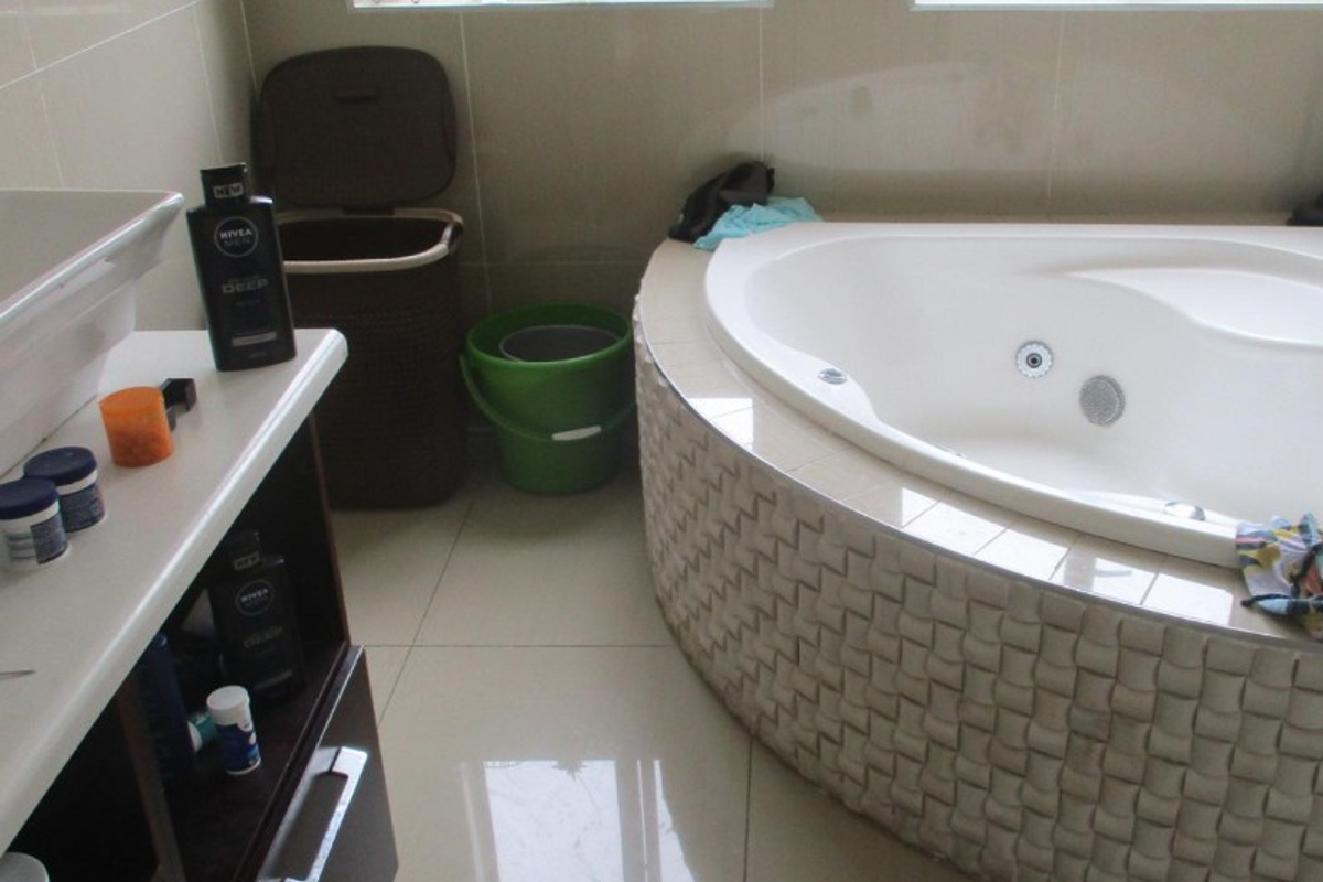 A bathroom featuring a built-in corner bathtub with a decorative tiled surround, a vanity cabinet with a basin, and neutral wall and floor tiles.