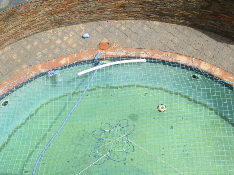 An elevated view of a circular swimming pool featuring stone cladding surround, paved decking, and a fitted safety net.