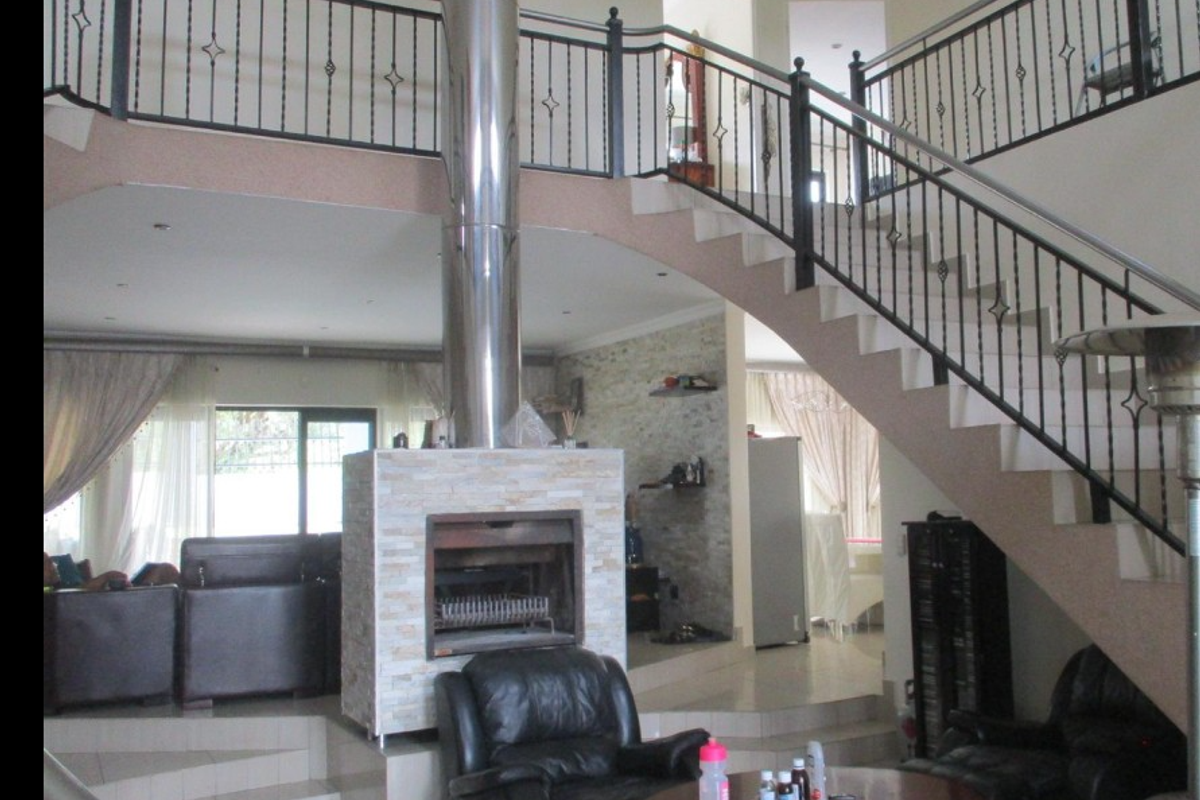 Spacious open-plan living area featuring a central stone-clad fireplace with a stainless steel flue and an elegant staircase leading to a mezzanine level.