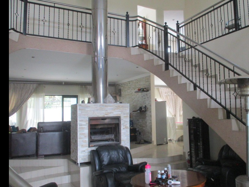 Spacious open-plan living area featuring a central stone-clad fireplace with a stainless steel flue and an elegant staircase leading to a mezzanine level.