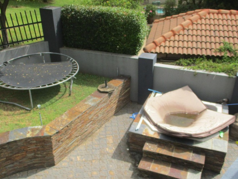 Rear outdoor area featuring a paved patio, stone-clad retaining walls, and a built-in spa with a boundary wall and metal fencing.