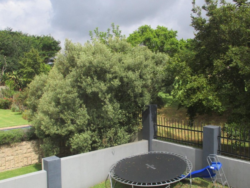 A private garden area featuring a well-maintained lawn, concrete boundary walls, and secure metal perimeter fencing with mature trees.
