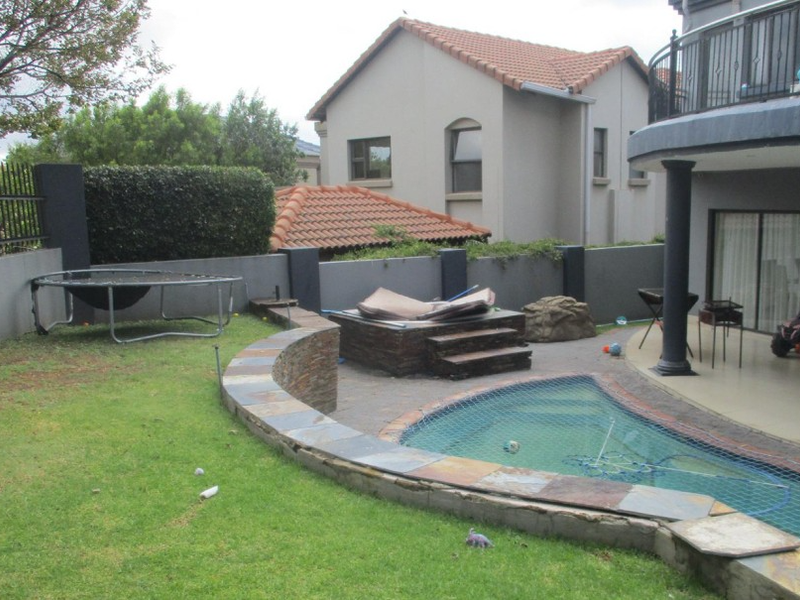 Outdoor entertainment area featuring a swimming pool, built-in jacuzzi, stone-clad retaining wall, and a covered patio space.