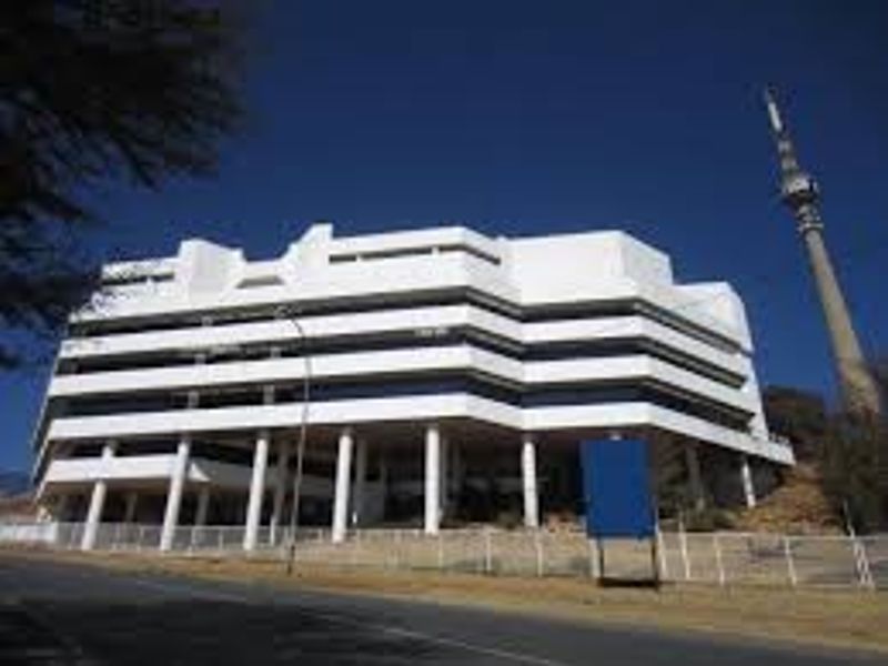 A multi-story commercial office building featuring a prominent white facade with ribbon windows and structural concrete pillars, viewed from the street level.
